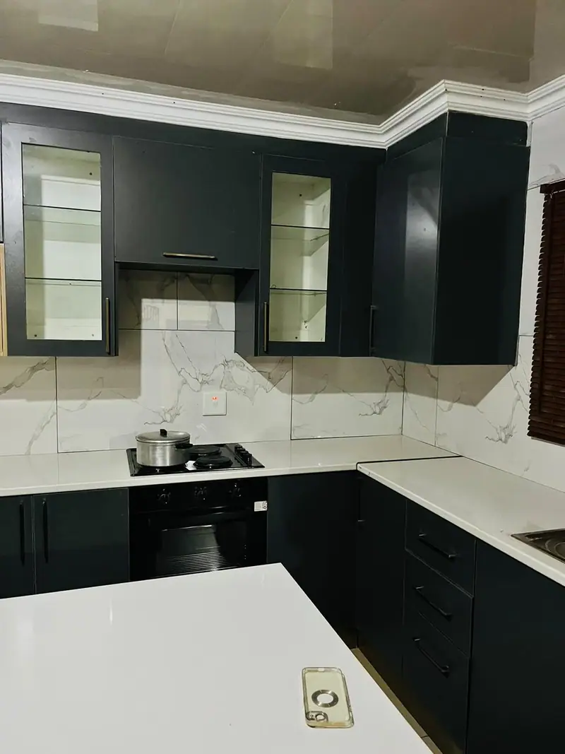 L-shaped charcoal kitchen with marble-effect wall tiles and white worktops