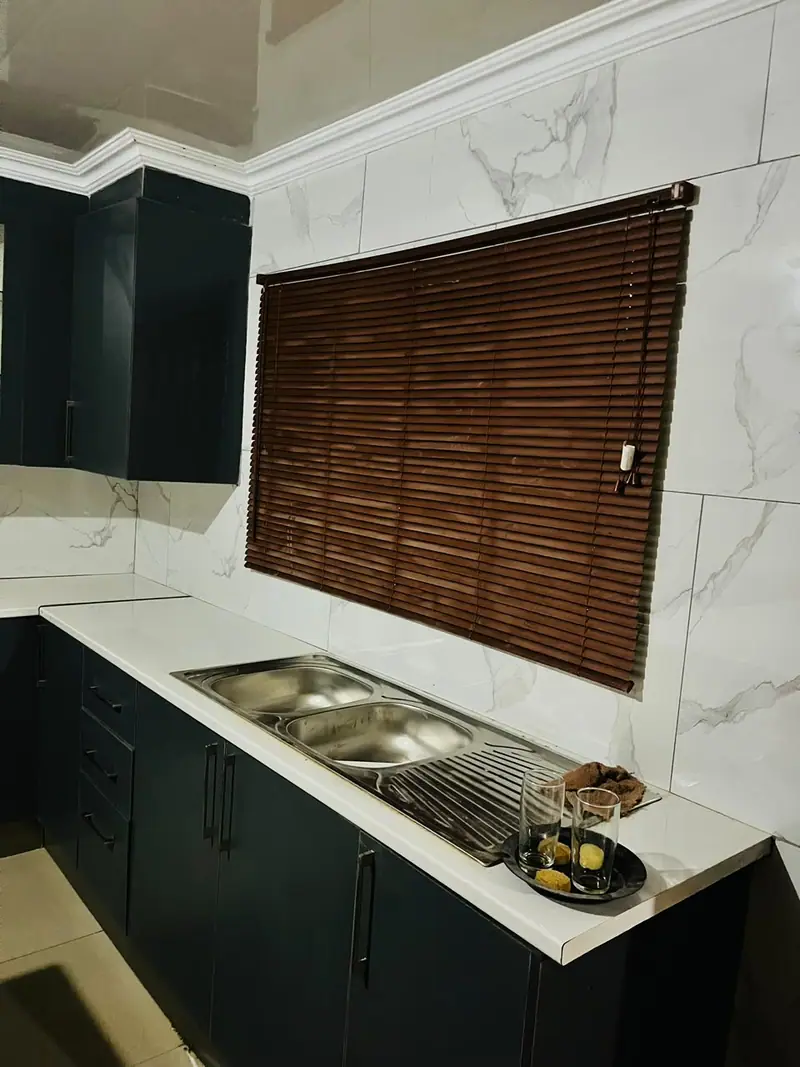 Charcoal cabinets around a stainless double sink under a timber blind