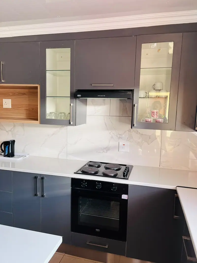 Charcoal kitchen with glass-front wall cabinets, a timber-framed shelf and a white worktop