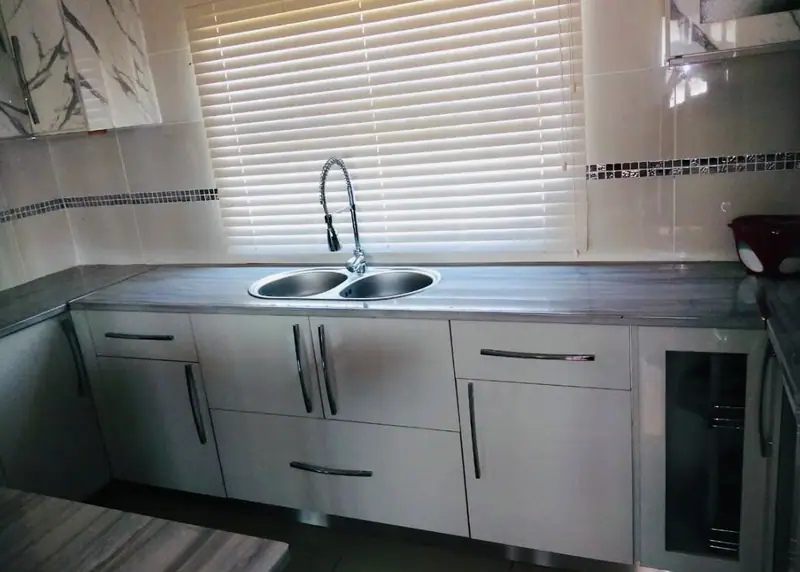 Light grey base cabinets with a double sink under a window blind