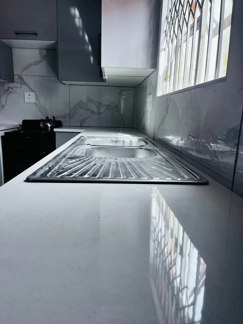 Stainless sink set in a grey worktop beside marble-effect tiles
