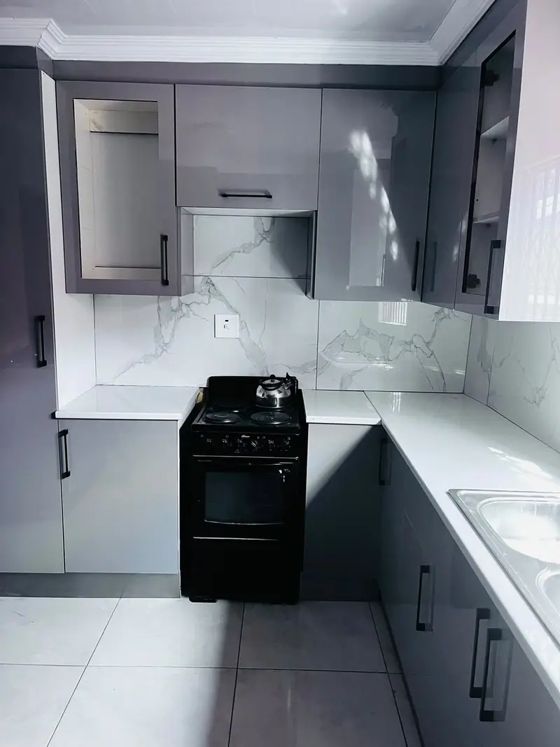 Grey high-gloss kitchen with a marble-effect splashback and a black freestanding stove