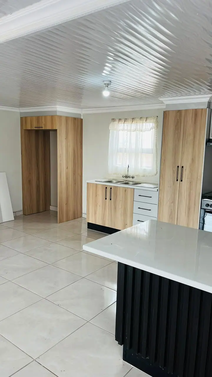 Open-plan kitchen with light timber-effect tall units and a black fluted island