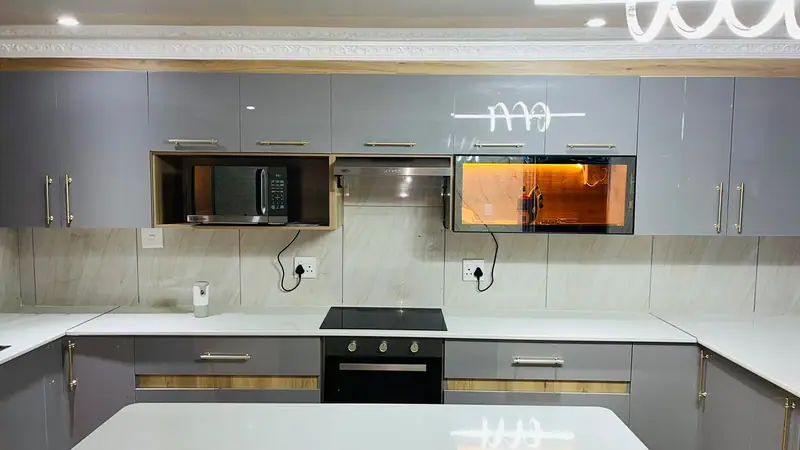 Wall of grey high-gloss cabinets with gold handles, timber trim and a built-in oven