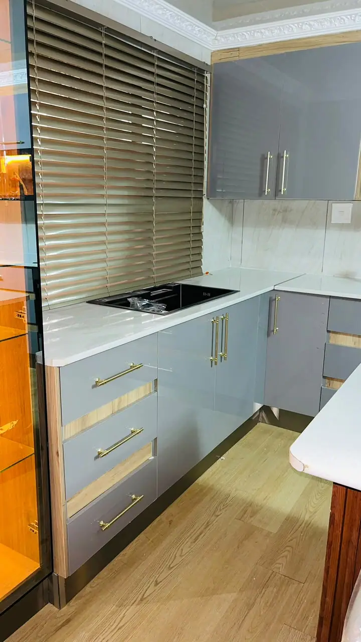 Grey drawer unit with gold handles beside a tall lit display cabinet